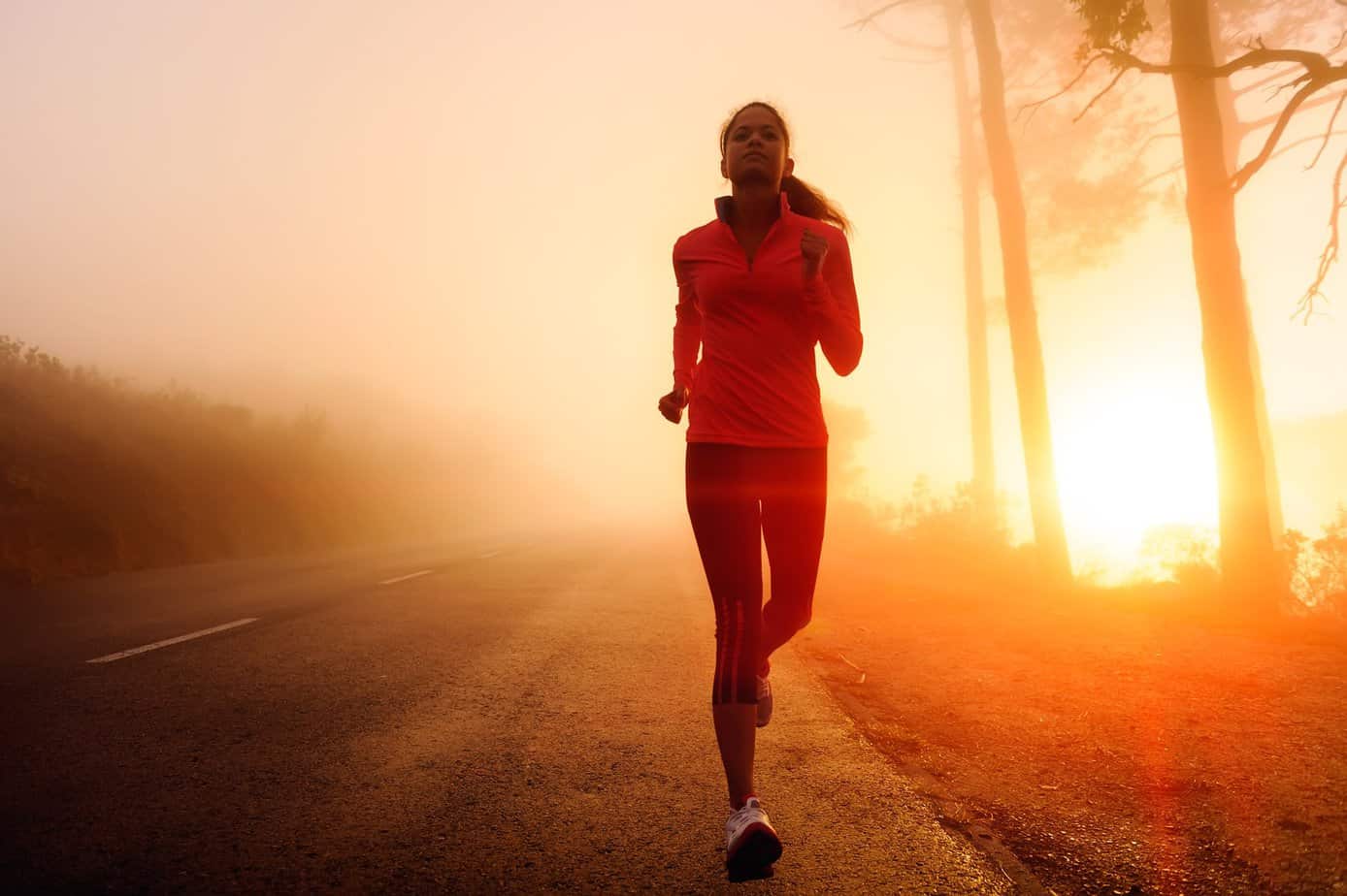 Healthy running runner woman early morning sunrise workout on misty mountain road workout jog. sunflare through the mist gives atmospheric feel and depth
